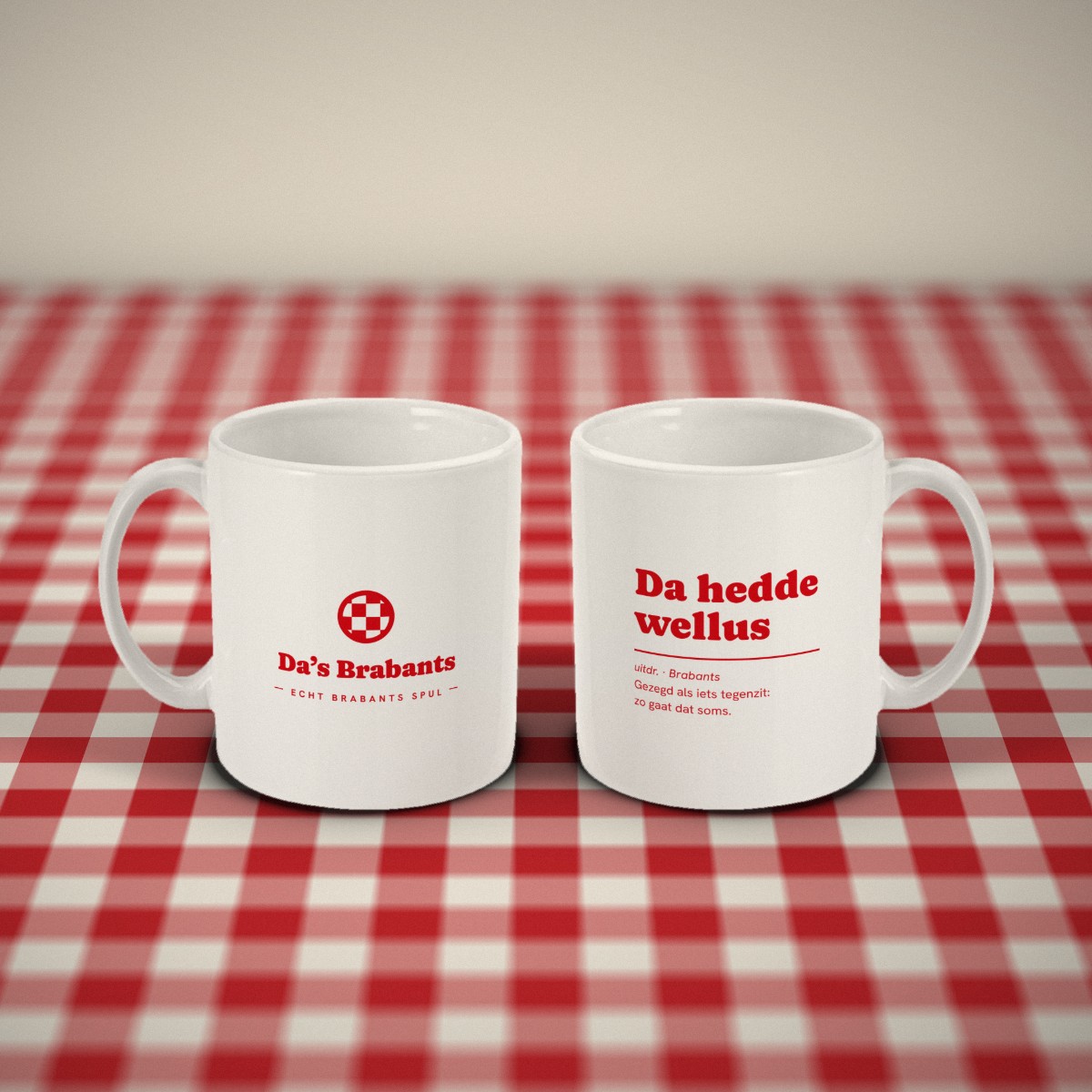 Voor- en achterkant: twee witte mokken „Da hedde wellus” naast elkaar op een rood-wit geruit tafelkleed