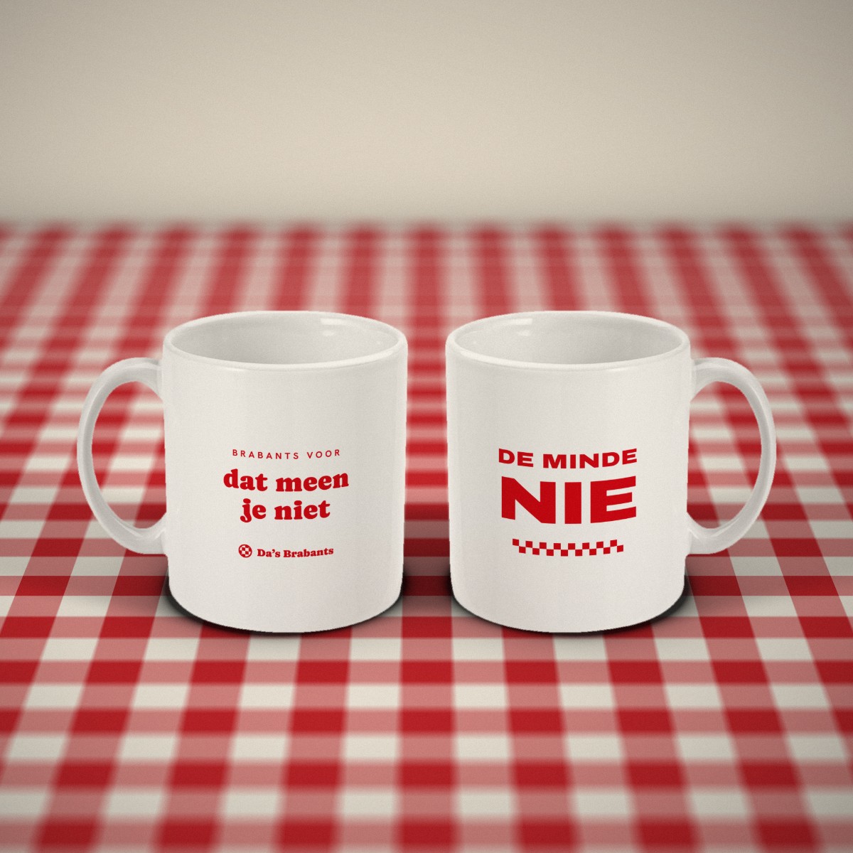 Voor- en achterkant: twee witte mokken „De minde nie” naast elkaar op een rood-wit geruit tafelkleed