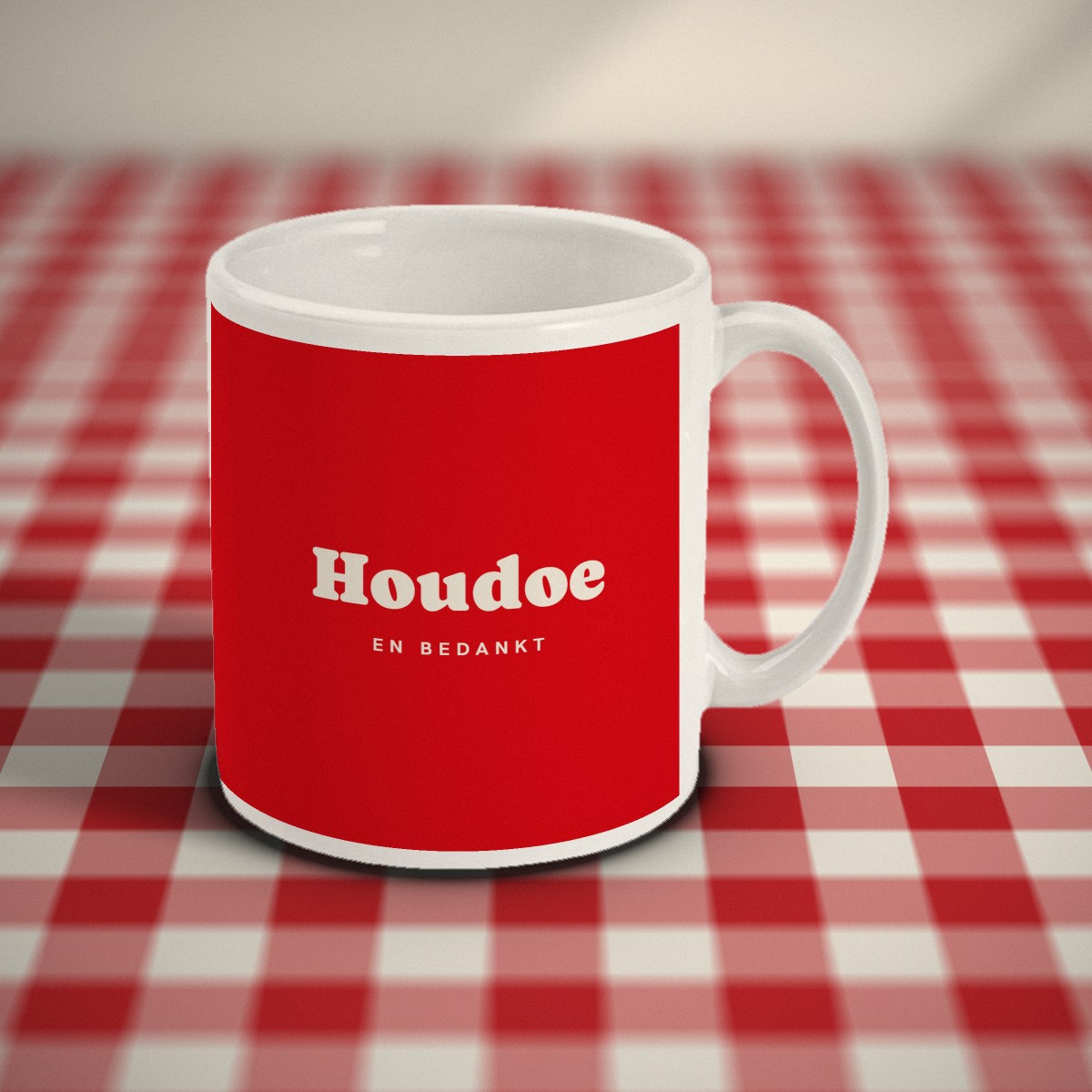 Voorkant: rode mok met in crème letters „Houdoe” en daaronder „en bedankt”, op een rood-wit geruit tafelkleed