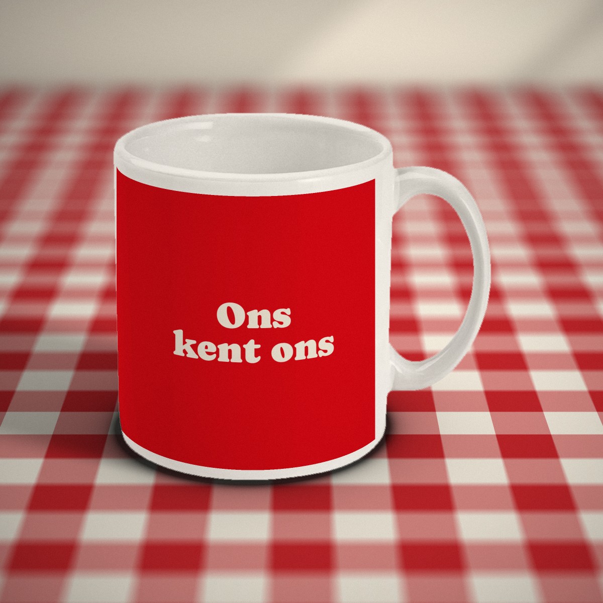 Voorkant: rode mok met in crème letters „Ons kent ons”, op een rood-wit geruit tafelkleed