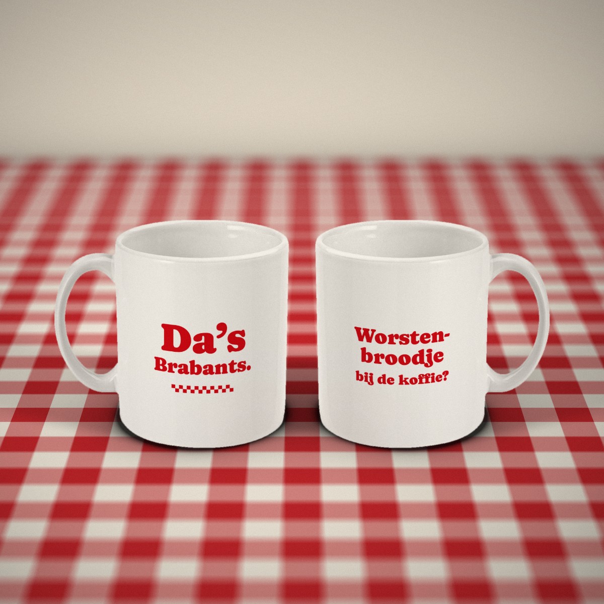 Voor- en achterkant: twee witte mokken „Worstenbroodje bij de koffie?” naast elkaar op een rood-wit geruit tafelkleed